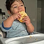 child, toddler, high_chair, bread, eating, crumbs, striped_clothing, indoor, face, hands, happy, food, meal, home, person, cute, baby, furniture, light, expression
