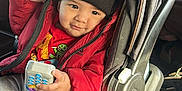 Milán is registered to the contest to win money with this photo: toddler, child, car_seat, red_jacket, black_beanie, toy_phone, indoor, smile, clothing, person, seatbelt, car_interior, cute, playful, winter_wear, young_child, sitting, hand, face, window