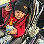 toddler, child, car_seat, red_jacket, black_beanie, toy_phone, indoor, smile, clothing, person, seatbelt, car_interior, cute, playful, winter_wear, young_child, sitting, hand, face, window