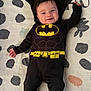 baby, batman_costume, cape, smiling, infant, black_clothing, blanket, pattern, lying_down, cute, child, portrait, happy, indoors, soft_texture, small_child, costume, superhero, black_socks, head
