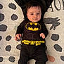 baby, infant, batman_costume, cape, black_clothing, lying_down, blanket, patterned_blanket, face, cute, child, superhero, costume, small_hands, black_socks, indoor, portrait, expression, young_child, adorable