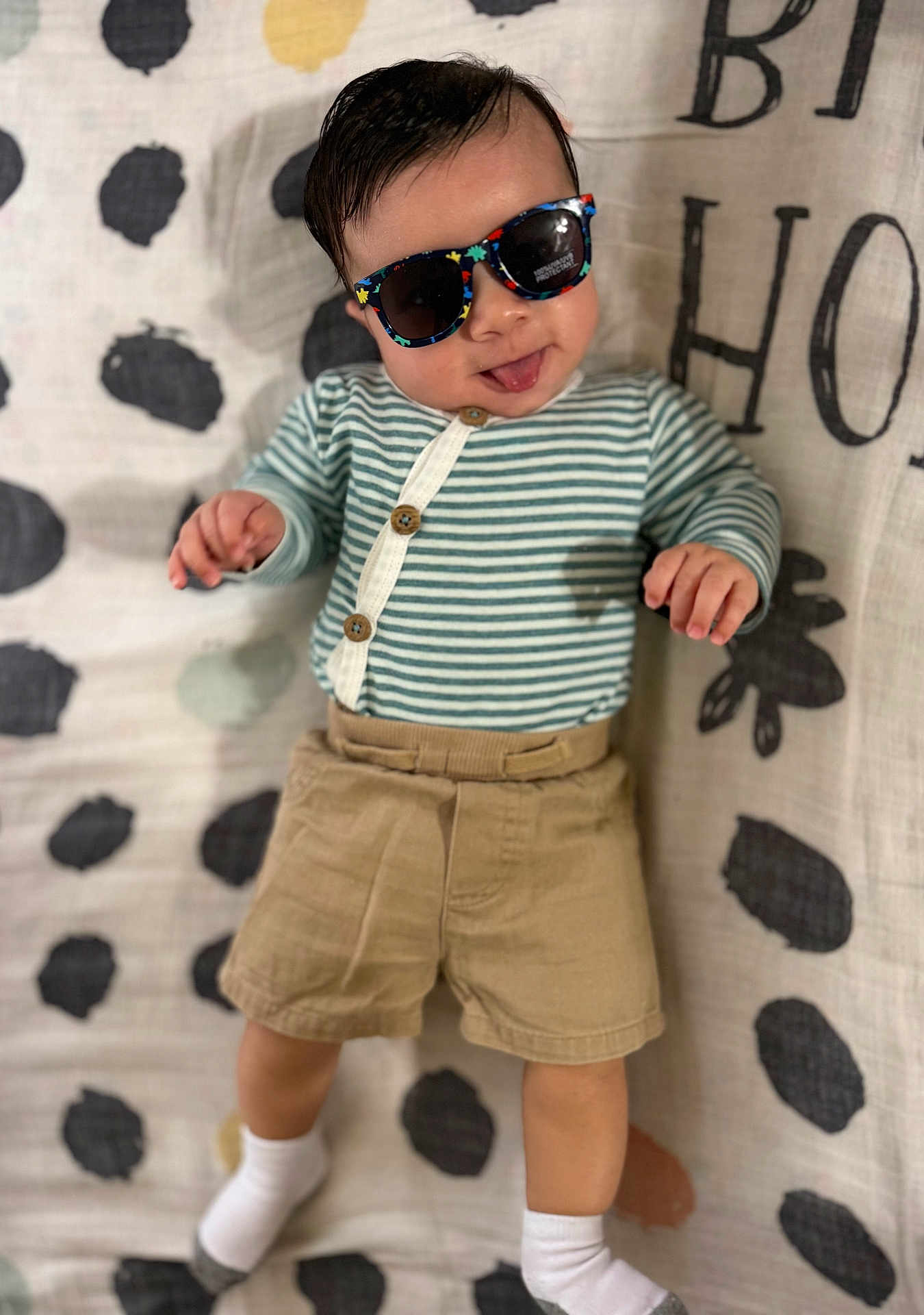Siul joined the competition — help win amazing prizes! baby, child, sunglasses, striped_shirt, khaki_shorts, white_socks, tongue_out, polka_dot_blanket, cute, playful, infant, lying_down, clothing, person, face, head, smile, hand, foot, patterned_background