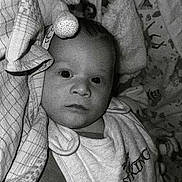 Léo participe au concours pour gagner de l'argent avec cette photo : baby, infant, blanket, soft_toy, clothing, bib, face, portrait, monochrome, black_and_white, bed, sleepwear, child, young, cute, expression, lying_down, cozy, indoor, text_overlay