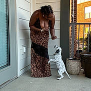 Duke joined the competition — help win amazing prizes! woman, dog, puppy, leopard_print, dress, porch, potted_plants, residential_building, concrete_floor, playful, interaction, animal, pet, standing, curly_hair, bracelets, door, window, outdoor, daylight