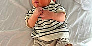 Joseph is registered to the contest to win money with this photo: newborn, baby, sleeping, infant, striped_shirt, shorts, bed, white_sheet, peaceful, hands, feet, skin, clothing, rest, cute, portrait, indoors, soft_light, child, relaxation