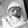 newborn, baby, sleeping, blanket, hat, wrapped, infant, cozy, soft, peaceful, closeup, portrait, monochrome, black_and_white, resting, cute, child, indoors, serene, calm