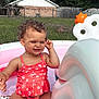 Everleigh is registered to the contest to win money with this photo: toddler, child, swimsuit, pool, inflatable_pool, outdoor, grass, house, summer, water, sunlight, playful, curly_hair, sitting, nature, daytime, fun, happy, vacation, backyard