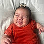 baby, smiling, infant, orange_dress, bow, happy, lying_down, cute, child, face, skin, hand, hair, portrait, white_background, clothing, person, funny_expression, closeup, indoors