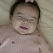 Iris a rejoint le concours — aidez-le/la à gagner de superbes lots ! baby, smiling, pink_bow, pink_sweater, knitted, flower_embroidery, close_up, face, happy, child, infant, cute, soft_lighting, indoors, portrait, lying_down, head_accessory, cheerful, young_child, person