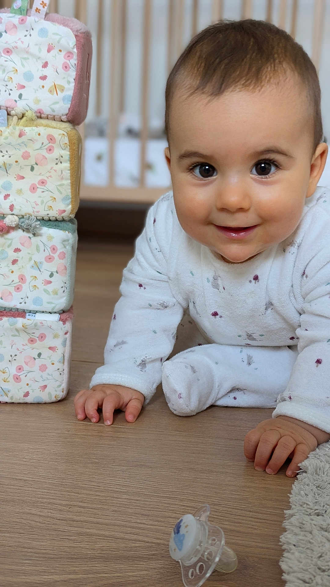 Albane participe au concours pour gagner de l'argent avec cette photo : baby, crawling, pajamas, floor, pacifier, toys, blocks, soft_toys, crib, wooden_floor, smiling, child, indoor, cute, face, hand, infant, home, comfort, playtime