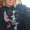 person, dog, puppy, black_and_white_dog, hoodie, sunglasses, car_interior, seat, window, smiling, face, pet, cute, ears, close_up, casual, young_adult, portrait, indoor, human