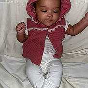 Ena is registered to the contest to win money with this photo: baby, child, infant, hooded_vest, maroon_clothing, lace_trim, white_pants, sitting, barefoot, indoors, fabric_backdrop, cute, calm, curious, skin, face, hands, foot, portrait, person