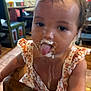 toddler, child, messy, food, tongue_out, high_chair, indoor, wooden_furniture, dress, curly_hair, face, playful, brown_eyes, table, chair, floor, person, cute, baby, dining_area