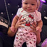 Shaniya is registered to the contest to win money with this photo: baby, bedroom, carpet, child, clothing, couch, curly_hair, cute, face, hands, headband, hello_kitty, indoor, infant, pajamas, person, purple_light, sitting, smile, support