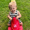 Beckham is registered to the contest to win money with this photo: blonde_hair, child, face, fun, grass, grass_field, greenery, hands, happy, outdoor, play, playground, red_toy, slide, smiling, striped_clothing, summer, sunlight, toddler, toy_vehicle