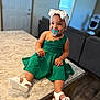 toddler, child, green_dress, white_sandals, headband, pacifier, smiling, indoor, marble_countertop, living_room, furniture, happy, cute, baby, person, footwear, accessories, home, portrait, sitting