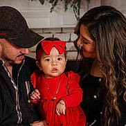 Sophia is registered to the contest to win money with this photo: baby, child, woman, man, family, red_dress, headband, portrait, indoor, smile, love, holiday_decor, greenery, jewelry, casual_clothing, hat, long_hair, holding, people, warmth