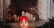 Sophia is registered to the contest to win money with this photo: baby, child, red_dress, headband, fireplace, candles, indoor, portrait, cute, holiday, festive, smiling, sitting, floor, decor, warm_lighting, accessory, jewelry, sock, holiday_season