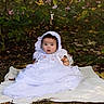 baby, child, infant, white_dress, lace, bonnet, outdoor, nature, foliage, blanket, grass, leaves, portrait, cute, sitting, young, person, face, expression, curious