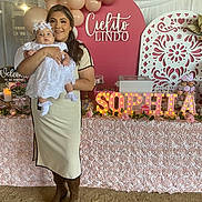 Sophia is registered to the contest to win money with this photo: woman, baby, balloons, party, celebration, baptism, white_dress, lace, sign, lighting, table, decorations, flowers, boots, smile, indoor, event, pink, happy, portrait