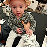baby, child, hat, floral_shirt, white_pants, hand, table, chairs, indoor, person, face, curious, seated, napkin, cutlery, salt_shaker, pepper_shaker, number_sign, dining, casual