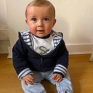Eyden participe au concours pour gagner de l'argent avec cette photo : baby, child, toddler, sitting, wooden_floor, white_wall, blue_jacket, striped_shirt, jeans, white_socks, hands, face, big_eyes, blond_hair, portrait, indoor, cute, looking_up, smile, floorboard