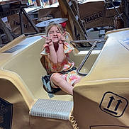 Lou participe au concours pour gagner de l'argent avec cette photo : child, girl, smiling, amusement_park, ride_vehicle, fragile_sign, playful, wooden_structure, outdoor, casual_clothing, seatbelt, people, background, fence, hat, greenery, daylight, fun, gesture, happy