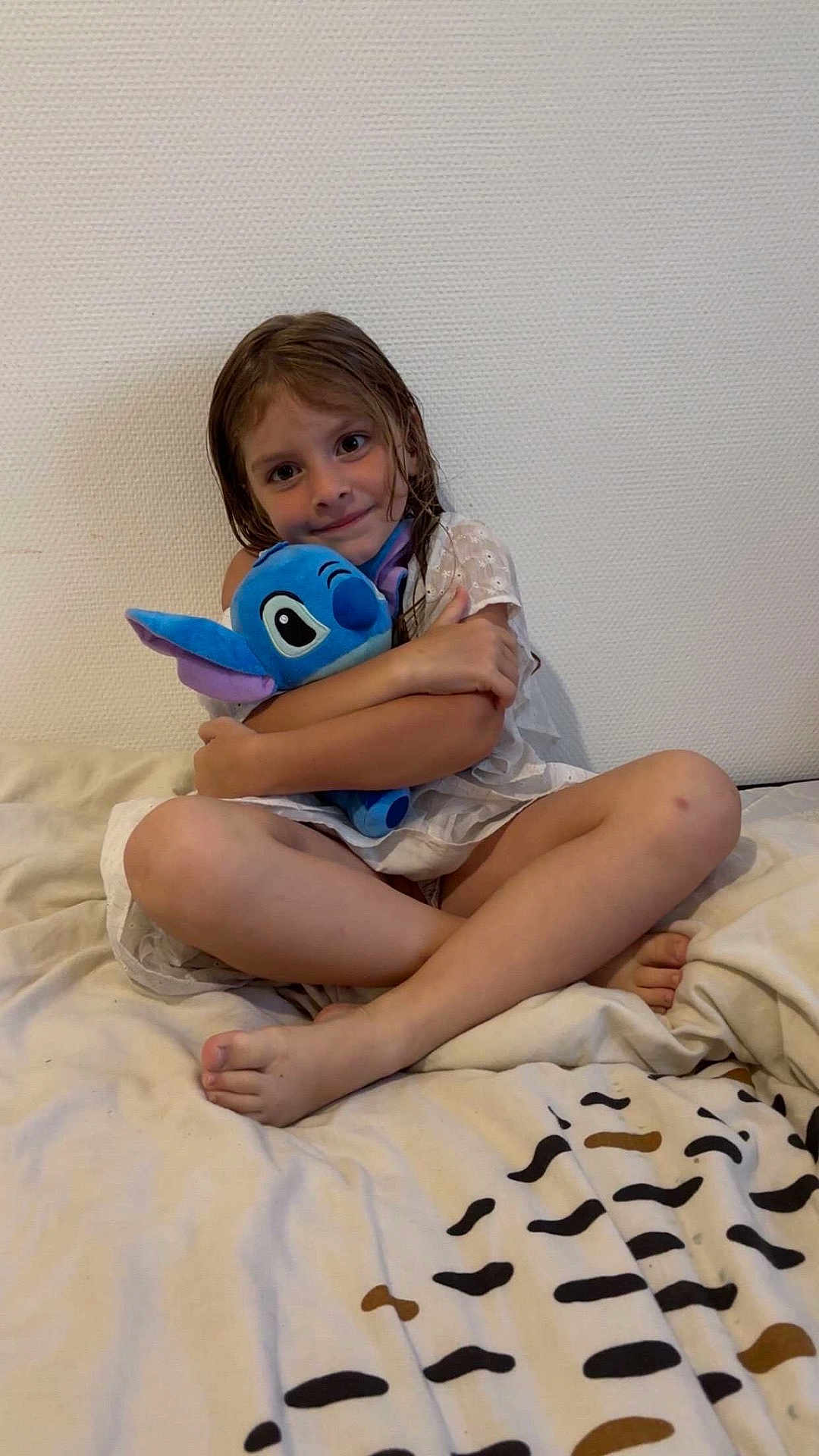 Lou a rejoint le concours — aidez-le/la à gagner de superbes lots ! child, toy, plush, stitch, bed, blanket, white_dress, smile, cross_legged, indoor, wall, barefoot, cute, hugging, young, person, happy, soft_toy, girl, cozy