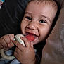 Juan joined the competition — help win amazing prizes! baby, teething_toy, smile, hand, blanket, face, infant, closeup, happy, child, skin, fingers, pillow, comfort, cute, young, expression, indoors, rest, holding