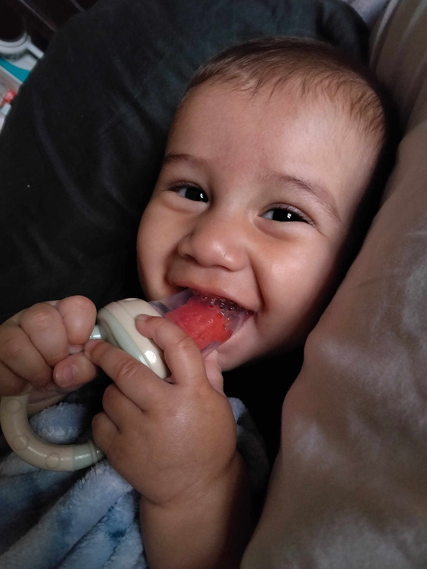 Juan joined the competition — help win amazing prizes! baby, teething_toy, smile, hand, blanket, face, infant, closeup, happy, child, skin, fingers, pillow, comfort, cute, young, expression, indoors, rest, holding