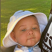 Zamari is registered to the contest to win money with this photo: baby, child, hat, bucket_hat, face, person, outdoor, greenery, grass, park, daylight, car, vehicle, sunlight, smile, carrier, clothing, shirt, closeup, expression
