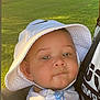 baby, child, hat, bucket_hat, face, person, outdoor, greenery, grass, park, daylight, car, vehicle, sunlight, smile, carrier, clothing, shirt, closeup, expression