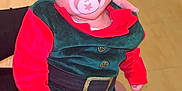 Rayan participe au concours pour gagner de l'argent avec cette photo : baby, infant, child, pacifier, elf_costume, red_clothing, green_clothing, striped_pants, holiday_outfit, indoor, person, face, headwear, sitting, hand, fabric, toy, furniture, bag, floor