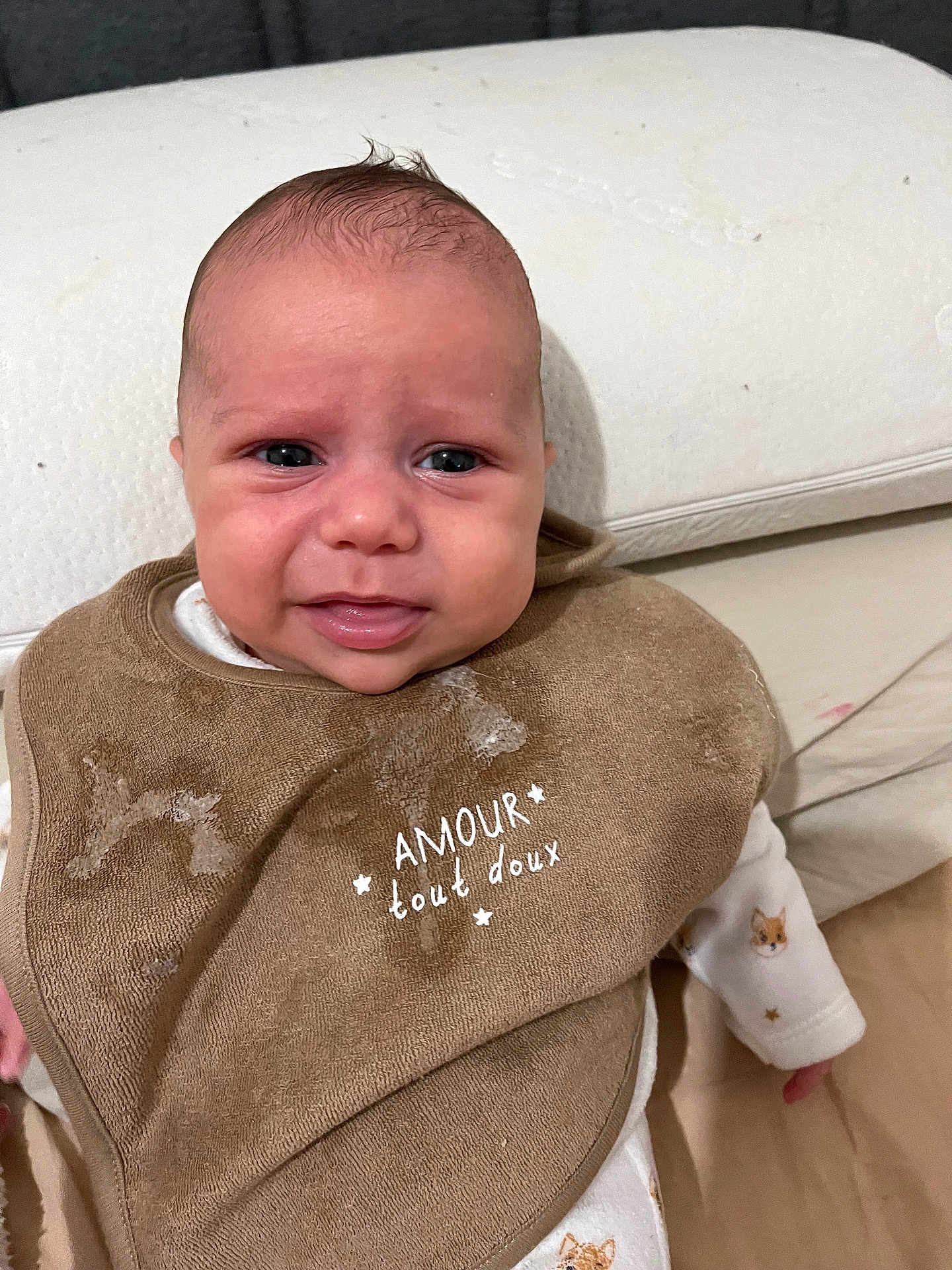 Rayan a rejoint le concours — aidez-le/la à gagner de superbes lots ! baby, infant, bib, brown_bib, white_outfit, fox_print, drool, face, expression, cushion, stain, sitting, indoors, child, cute, young, portrait, head, skin, clothing