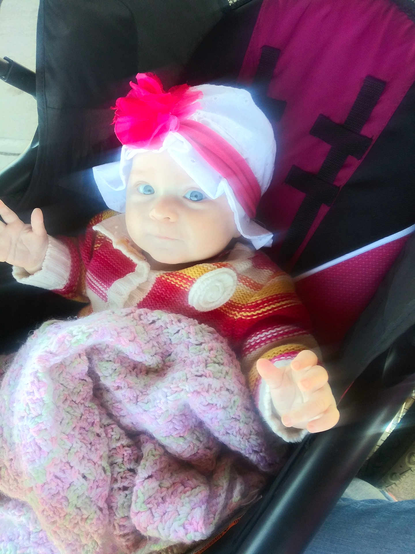 Maryanne is registered to the contest to win money with this photo: baby, child, stroller, hat, flower, blanket, knit, sweater, hand, face, blue_eyes, pink, white, red, striped, outdoor, person, seat, comfort, cute