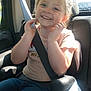 child, car_seat, seat_belt, smiling, happy, blonde_hair, jeans, pink_shirt, car_interior, window, daylight, safety, young_child, cute, portrait, casual_clothing, seat, person, vehicle, sunlight