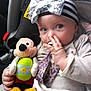 Maryanne is registered to the contest to win money with this photo: baby, child, car_seat, plush_toy, mickey_mouse, headband, pacifier, striped_clothing, toy, cute, indoor, seatbelt, infant, person, holding, colorful, soft_toy, hand, face, blue_eyes
