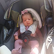 Alandra is registered to the contest to win money with this photo: infant, baby, car_seat, five_point_harness, bow, pink_outfit, onesie, newborn, car_interior, sunlight, shadow, seat, head_support, safety_label, hand, foot, face, eyes, portrait, cute