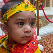Juhit joined the competition — help win amazing prizes! baby, child, infant, portrait, close_up, face, eyes, wide_eyed, headpiece, traditional_clothing, colorful, yellow, red, patterned_fabric, ceremonial, indoor, decorations, cultural_attire, looking_at_camera, festive