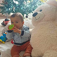 Enéa participe au concours pour gagner de l'argent avec cette photo : baby, child, child_playing, christmas_tree, cozy, cute, decorations, family, festive, holiday, holiday_season, indoor, ornaments, plush, smiling, soft_rug, teddy_bear, toy, window, winter