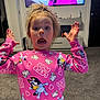 child, surprised, pink_shirt, unicorn, indoor, living_room, television, carpet, furniture, expression, person, young, casual_clothing, home, cute, funny_face, hands_up, hair_up, carpeted_floor, wall