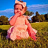 Nakiya is registered to the contest to win money with this photo: baby, child, infant, outdoor, grass, park, portrait, sitting, bow, headband, dress, pink_clothing, smiling, hand_to_mouth, curly_hair, face, sunlight, blue_sky, trees, nature