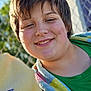 child, smiling, face, towel, colorful, outdoor, sunlight, green_shirt, happy, portrait, short_hair, casual, daylight, fence, background_blur, skin, young, person, nature, warm