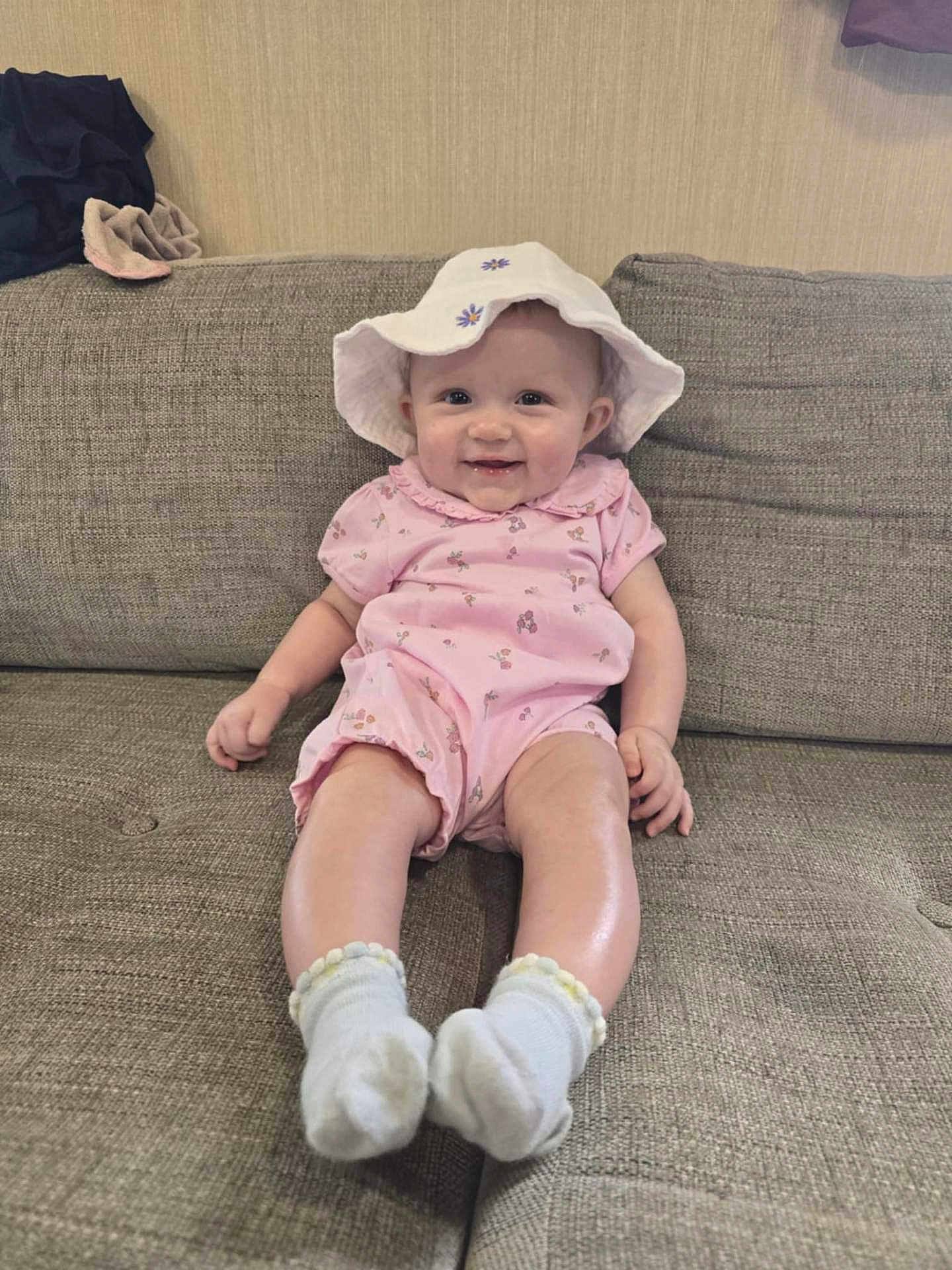 Emmie joined the competition — help win amazing prizes! baby, infant, smiling, pink_onesie, white_hat, socks, sofa, couch, indoor, child, cute, happy, portrait, seated, face, person, clothing, homedecor, furniture, baby_girl