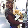 Nikko is registered to the contest to win money with this photo: woman, person, cat, orange_cat, white_cat, pet, smiling, glasses, long_hair, holding, animal, indoor, shopping_center, store, background, floor, casual_clothing, bracelet, portrait, candid