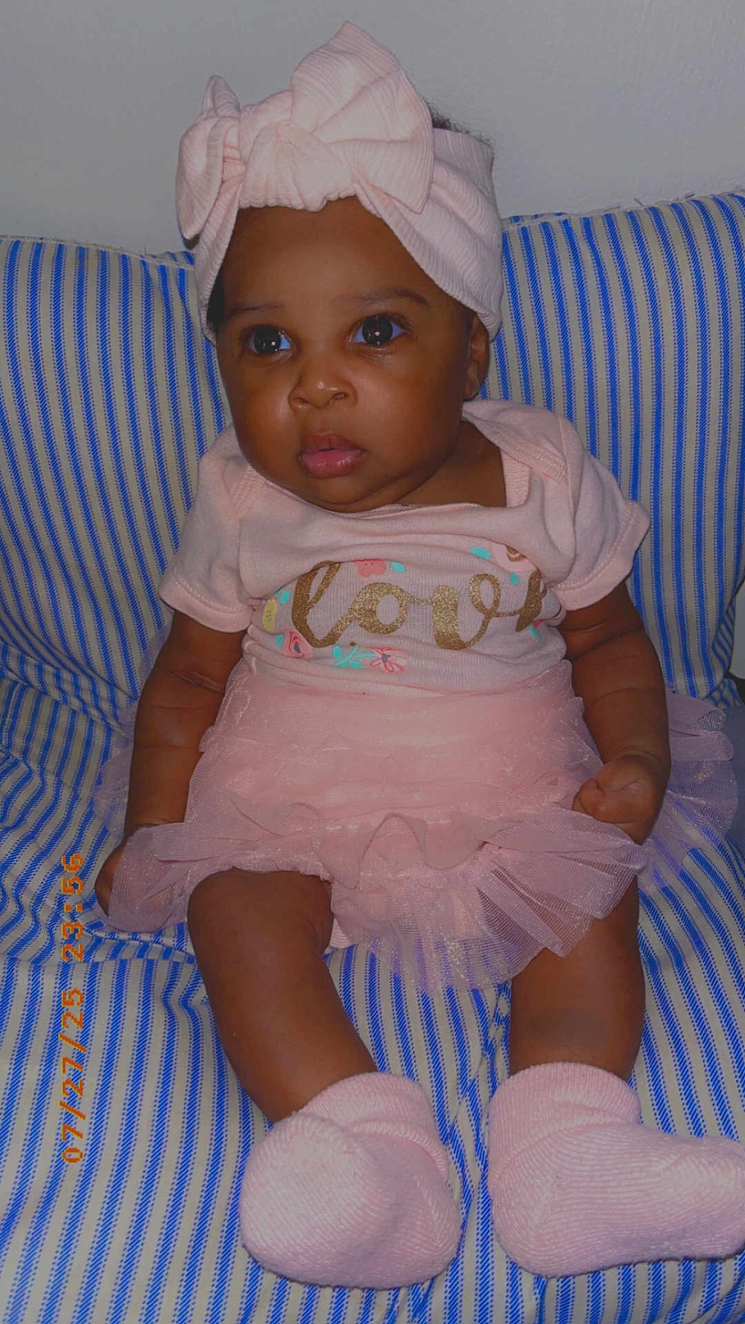 Malaysia is registered to the contest to win money with this photo: baby, child, pink_clothing, headband, bow, socks, striped_cushion, infant, cute, portrait, seated, soft_toys, indoor, small_child, adorable, expression, human, face, legs, curious