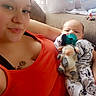 Jordan joined the competition — help win amazing prizes! woman, baby, pacifier, plush_toy, couch, orange_tank_top, pajamas, tattoo, indoor, curtains, window, relaxing, smiling, person, family, child, home, casual, comfort, portrait
