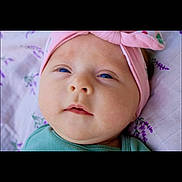 Gemma is registered to the contest to win money with this photo: baby, infant, face, headband, blue_eyes, pink, green_clothing, close_up, blanket, patterned, soft_lighting, lying_down, cute, child, newborn, portrait, skin, young, expression, indoors