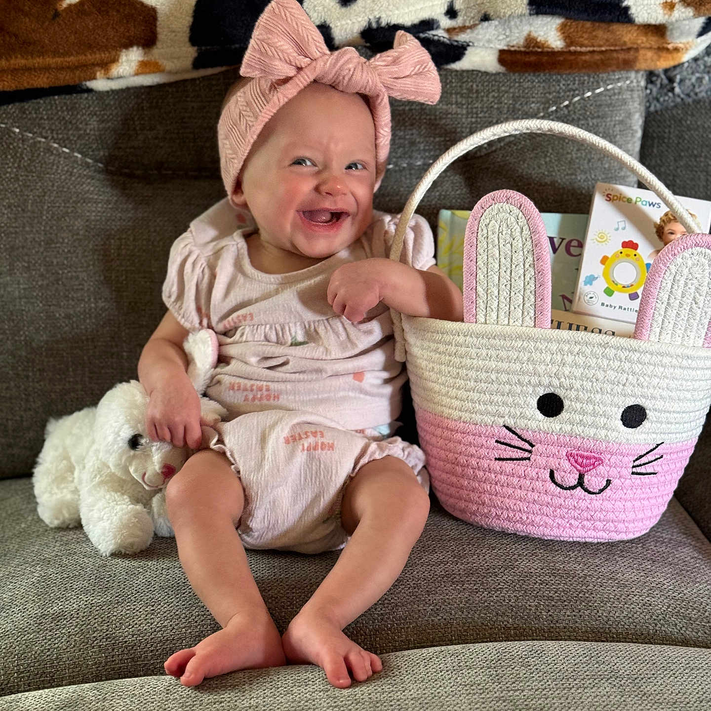 Sevaeh joined the competition — help win amazing prizes! baby, child, smiling, pink_bow, headband, stuffed_animal, plush_toy, basket, bunny_ears, books, couch, blanket, cow_print, happy, indoors, person, cute, infant, seated, cozy
