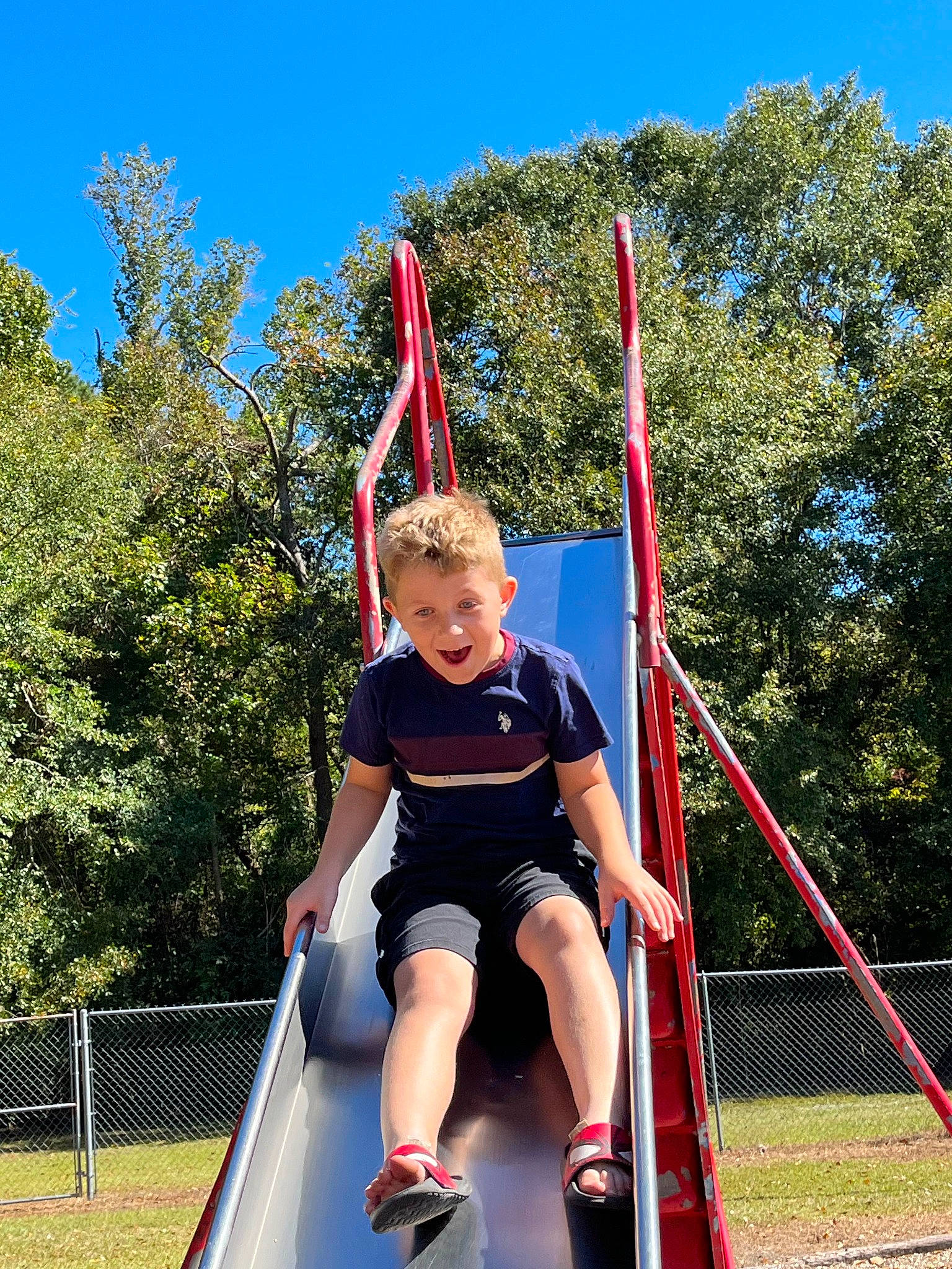Kolby is registered to the contest to win money with this photo: balance, chute, city, electric_blue, entertainment, fun, grass, leisure, outdoor_play_equipment, person, plant, playground, pole, recreation, shorts, sky, smile, t_shirt, toddler, trampolining_equipment_and_supplies